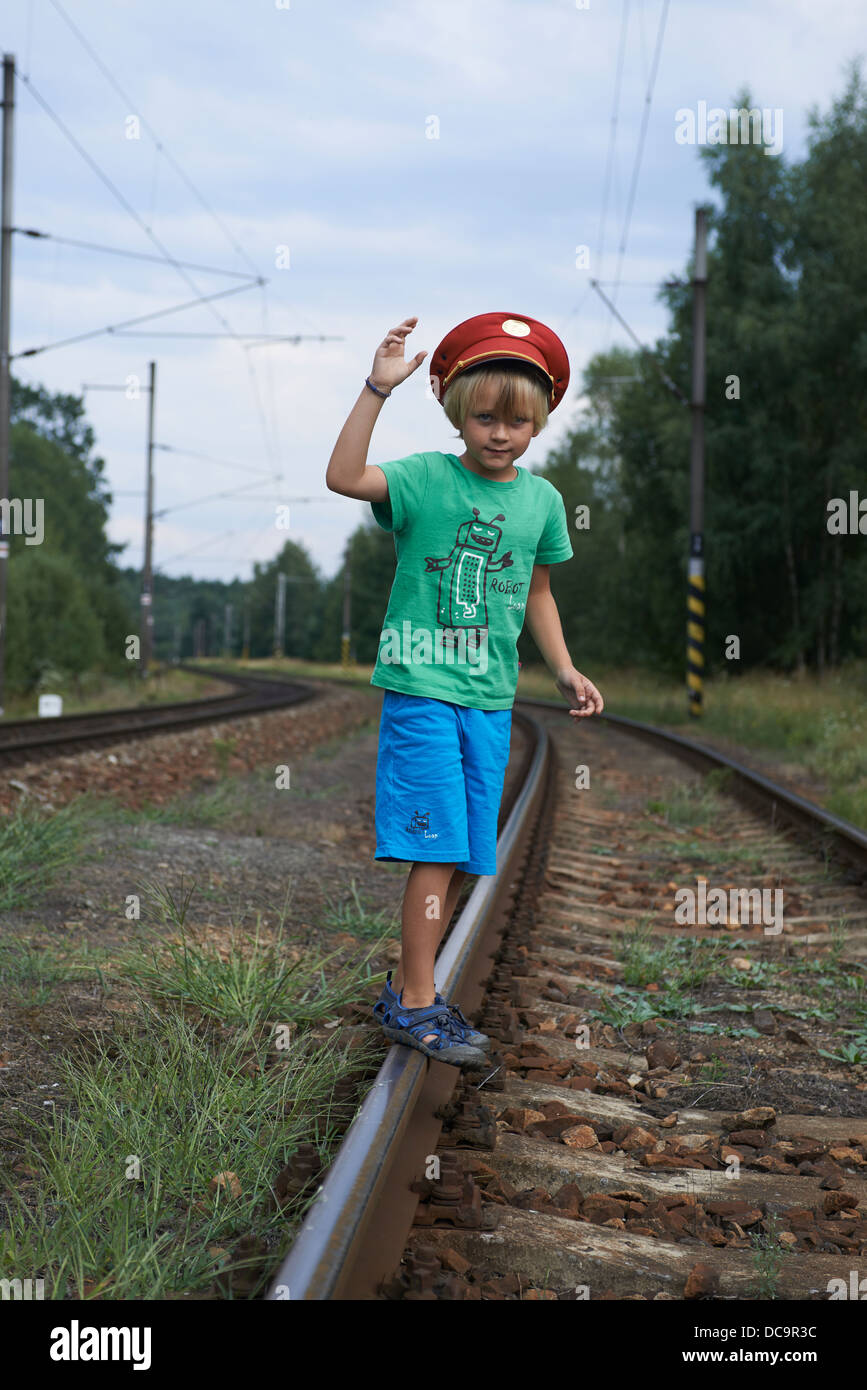 Child blond Boy with Train Dispatcher`s Cap playing in railway station